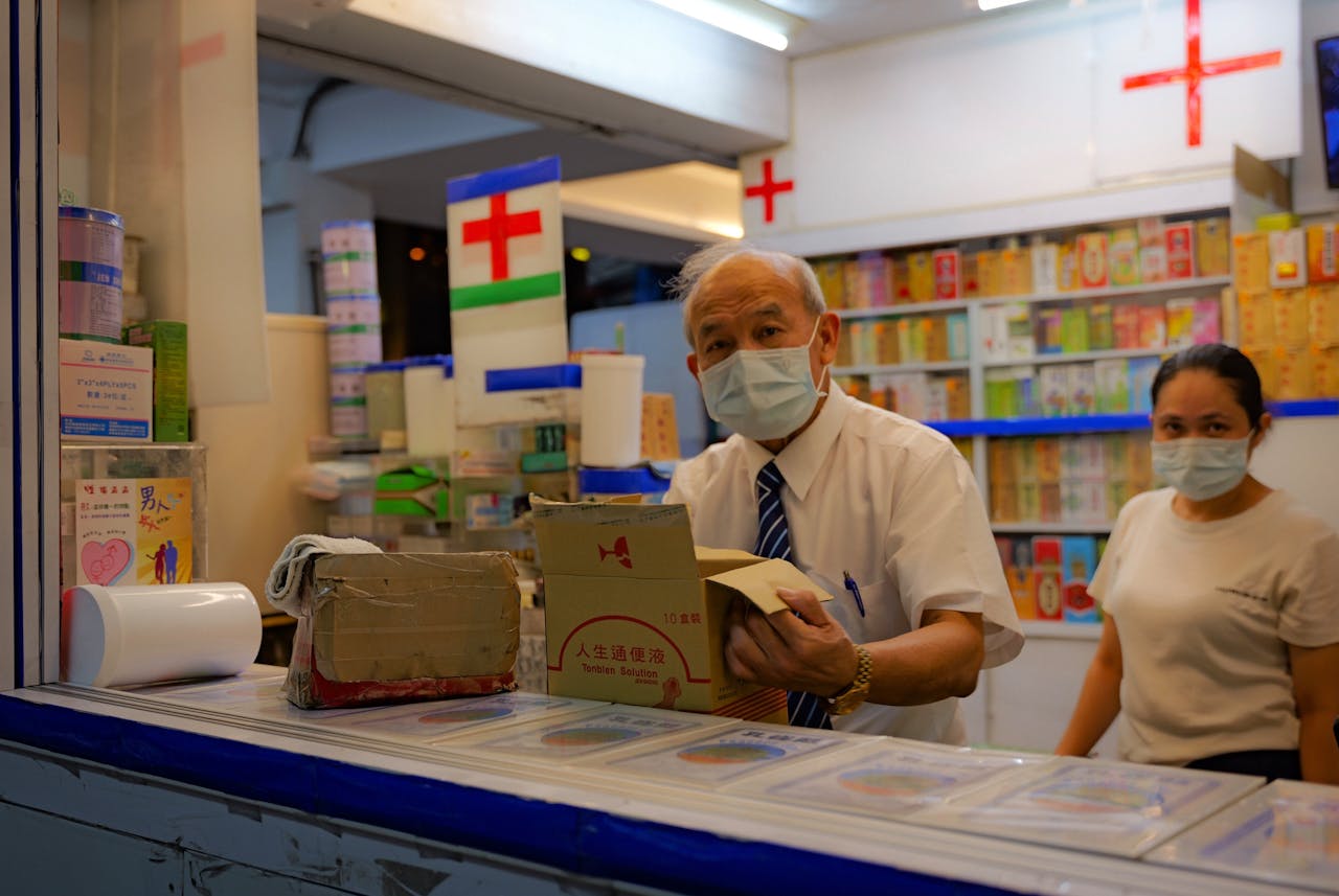 Two masked pharmacy workers organizing parcels in a Taitung pharmacy at night.