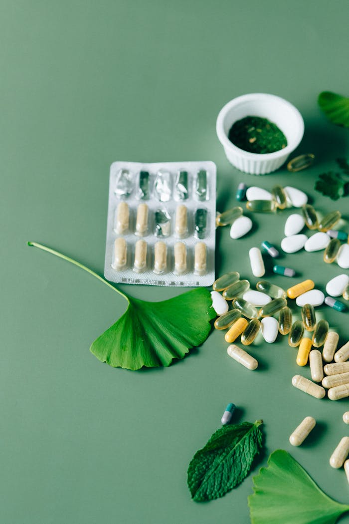 A flat lay of various natural supplements and capsules with herbs on a green surface.