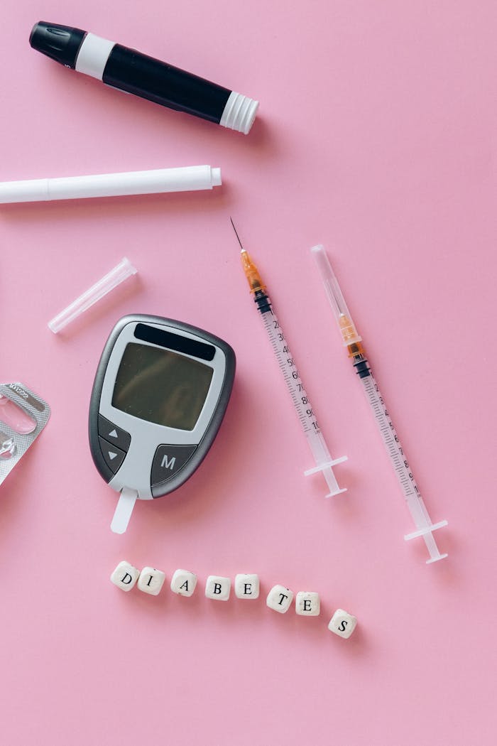 Close-up of diabetes monitoring tools with syringes and blocks spelling 'diabetes' on a pink background.